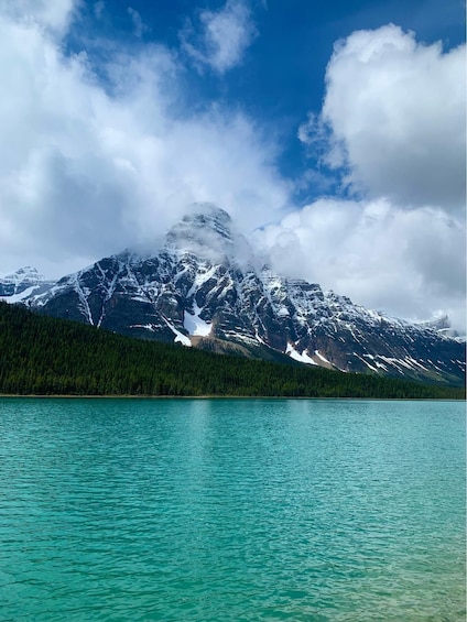 A mountain range with snow-capped peaks, a turquoise lake, and a forested area. 1