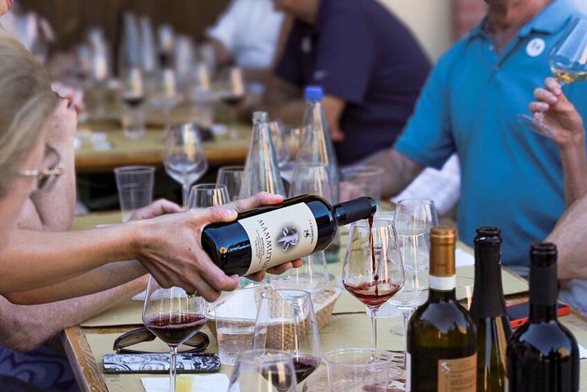 A person pouring wine into a glass at a table with multiple wine bottles and glasses. 1