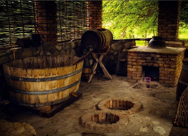 A rustic kitchen with a large wooden barrel, a brick oven, and two stone wells. 4