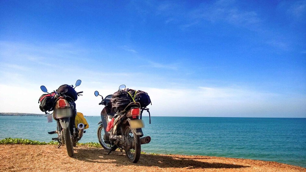 Two motorcycles parked by the sea with gear on them. 1