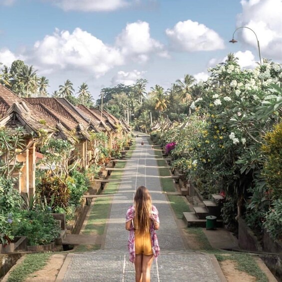 A woman walking down a pathway lined with traditional houses and lush tropical vegetation. 2