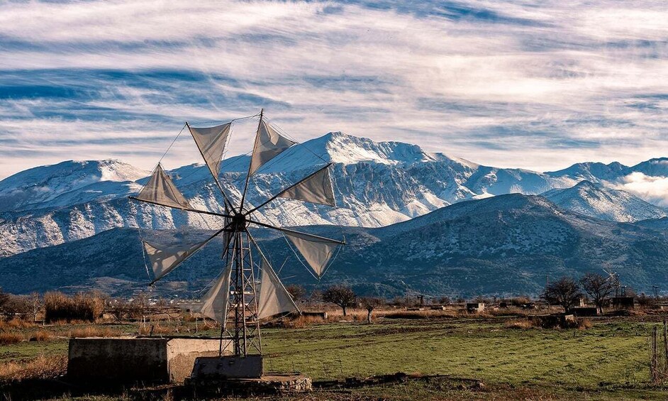Un molino de viento en un campo con montañas nevadas al fondo. 1