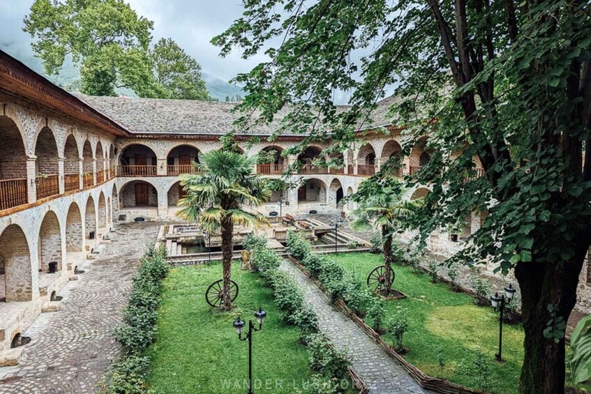 A courtyard with stone arches, a palm tree, and a pathway. 2