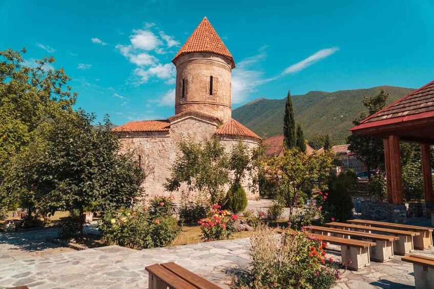 A historic church with a bell tower, surrounded by a garden with benches and flowering plants. 1
