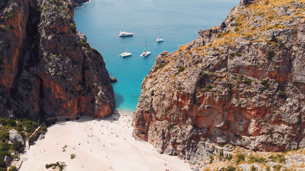 A coastal landscape with a beach, rocky cliffs, and several boats in the water. 3