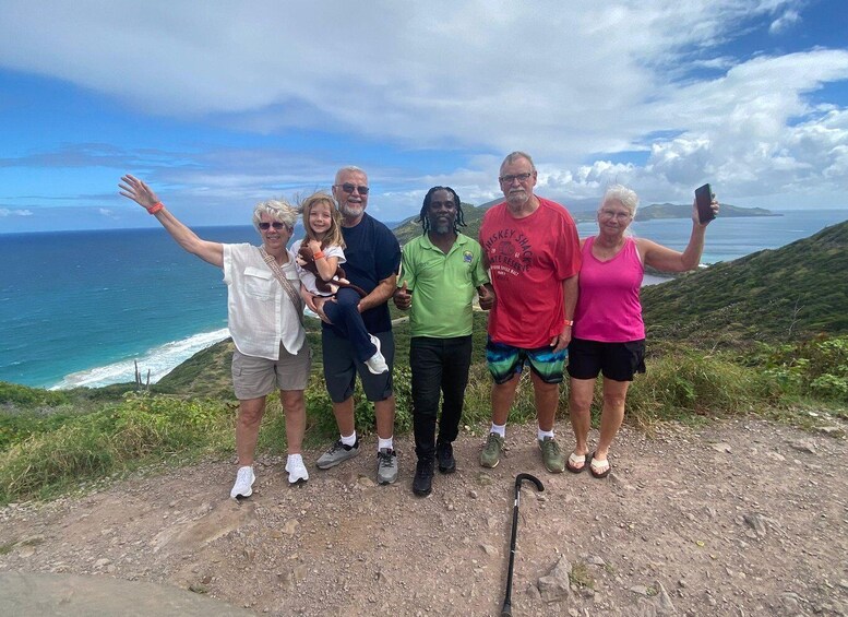 A group of people standing on a rocky hillside with a view of the ocean. 1