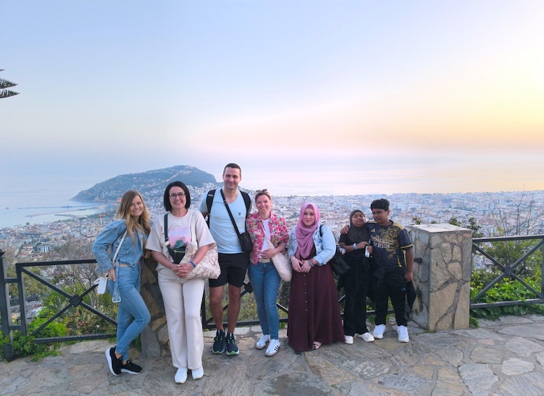 A group of people standing on a stone platform overlooking a cityscape with a distant mountain and a body of water. 4