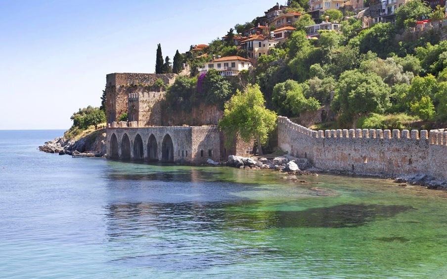 A coastal town with a historic stone wall and arches, overlooking a clear blue sea. 1