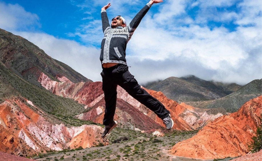 A person jumping in a mountainous landscape with red and green rock formations. 1