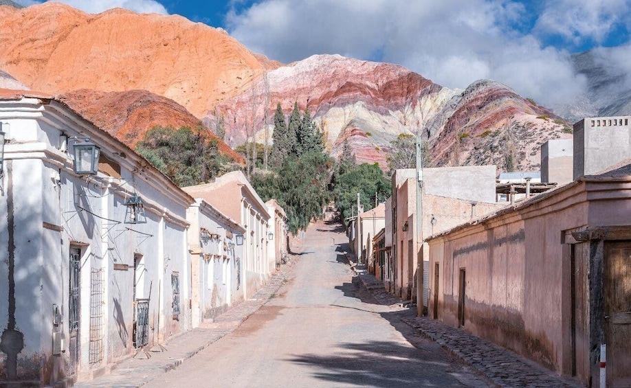 A narrow street flanked by buildings with a mountainous backdrop. 3