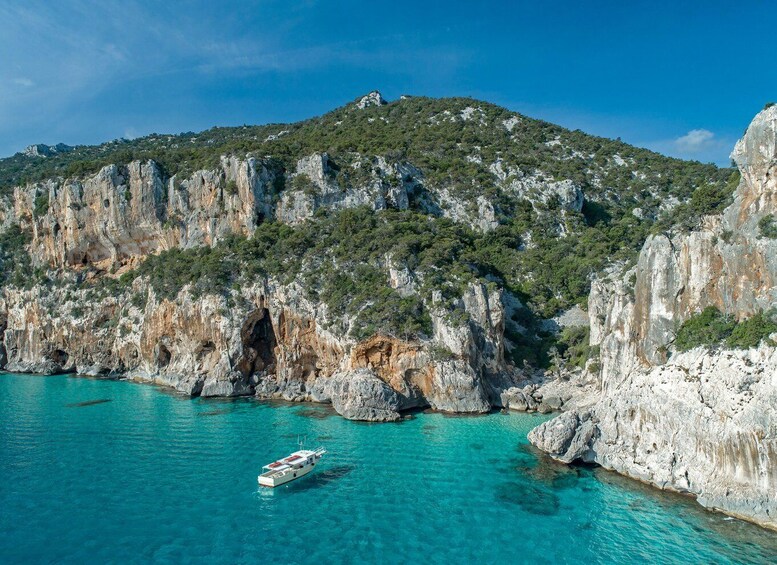 A boat on turquoise waters surrounded by rocky cliffs and a hill with sparse vegetation. 4