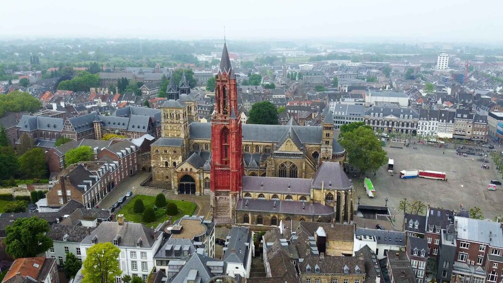 An aerial view of a historic town with a prominent red-towered church, surrounded by traditional buildings and a large open square. 5