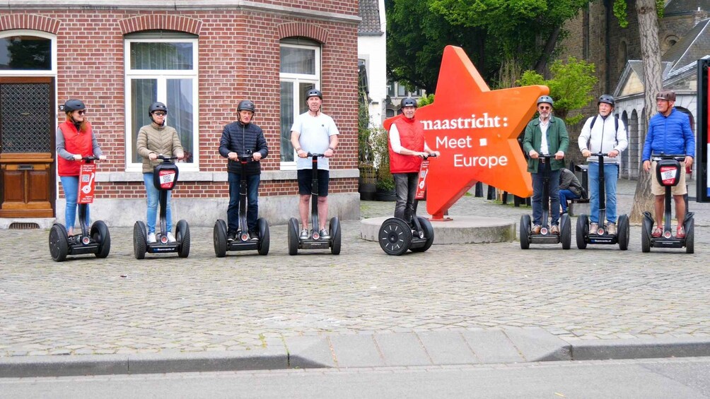 People riding segways on a cobblestone street with a large orange sign that reads "maastricht: Meet Europe". 3