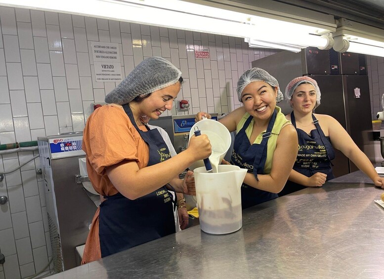 Three people in a kitchen, wearing hairnets and aprons, preparing food. 5