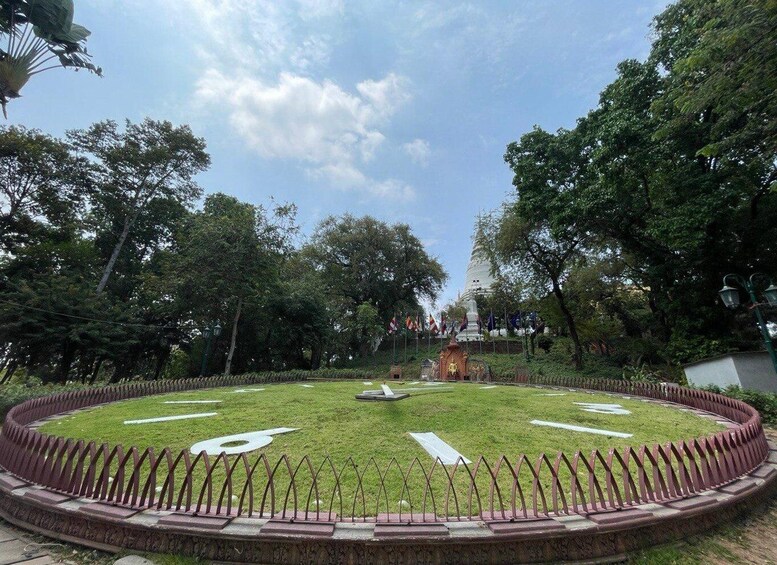 A circular garden with a central monument, surrounded by a fence and trees. 3