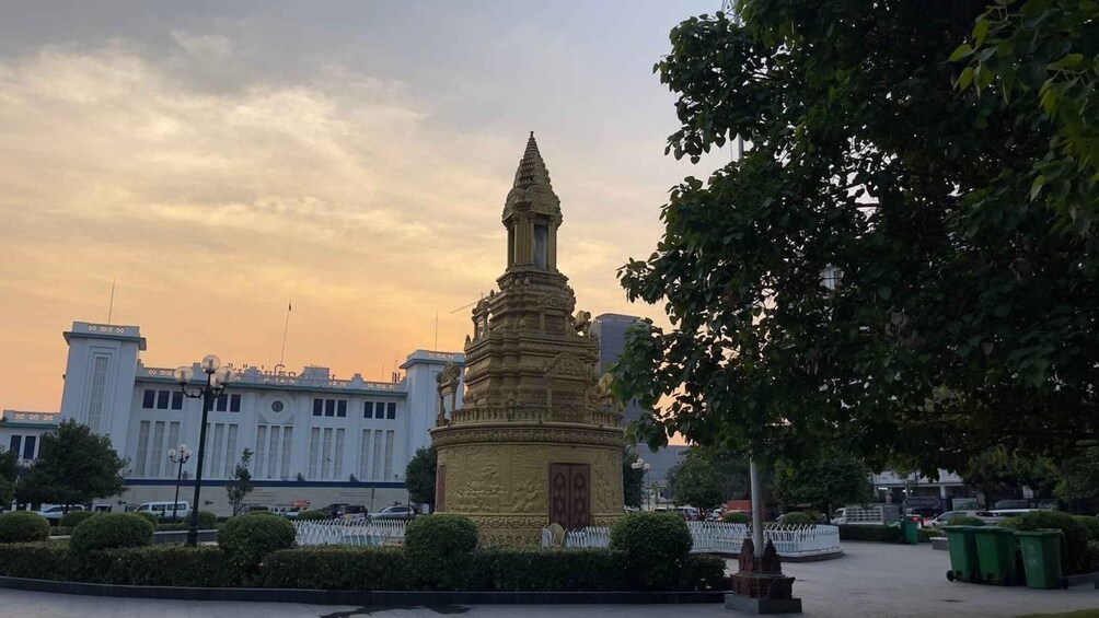 A golden stupa in a park with modern buildings in the background. 1