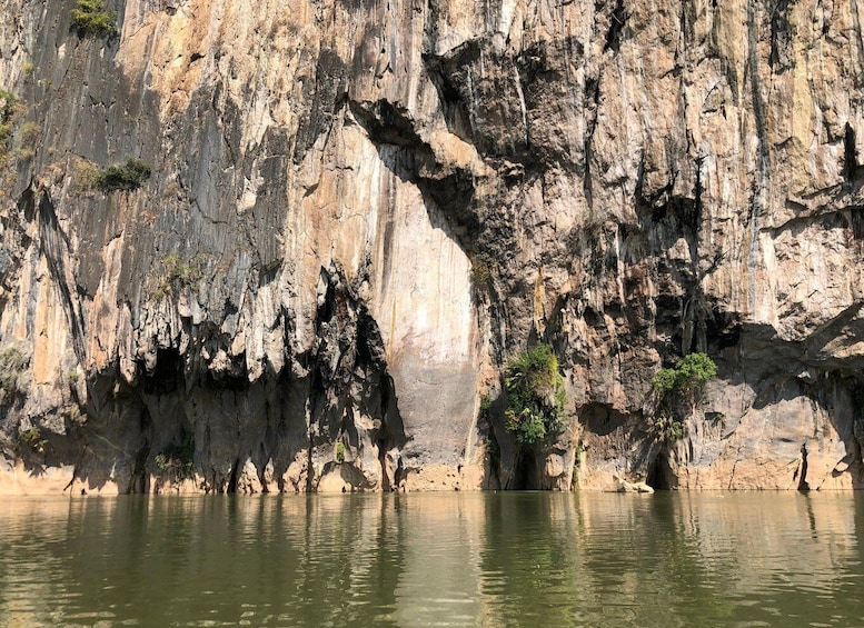 A limestone cliff with a large cave opening and a calm river at its base. 1