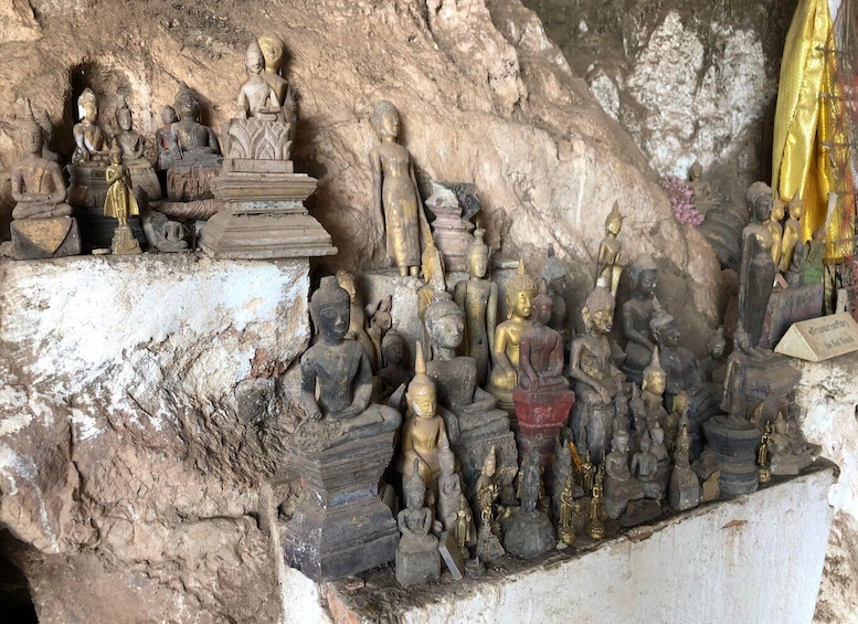 A collection of stone Buddha statues in various poses, some with gold accents, set against a rocky cave background. 2
