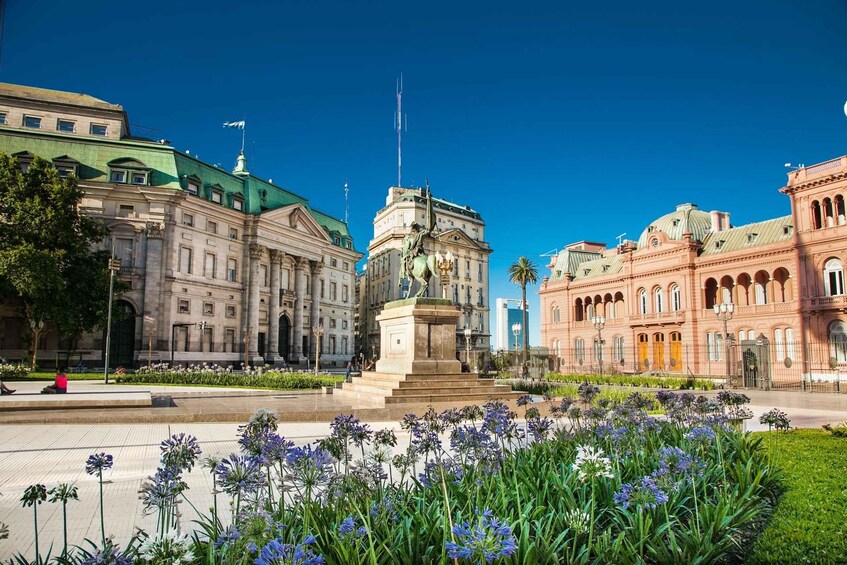 Una plaza con un monumento central, rodeada de arquitectura clásica y un jardín de flores. 1