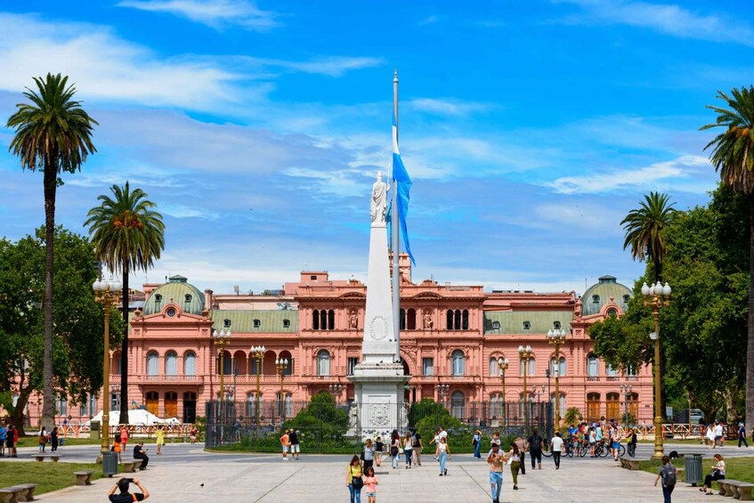 Una amplia plaza pública con un monumento central, palmeras y un edificio rosado con cúpulas. 3