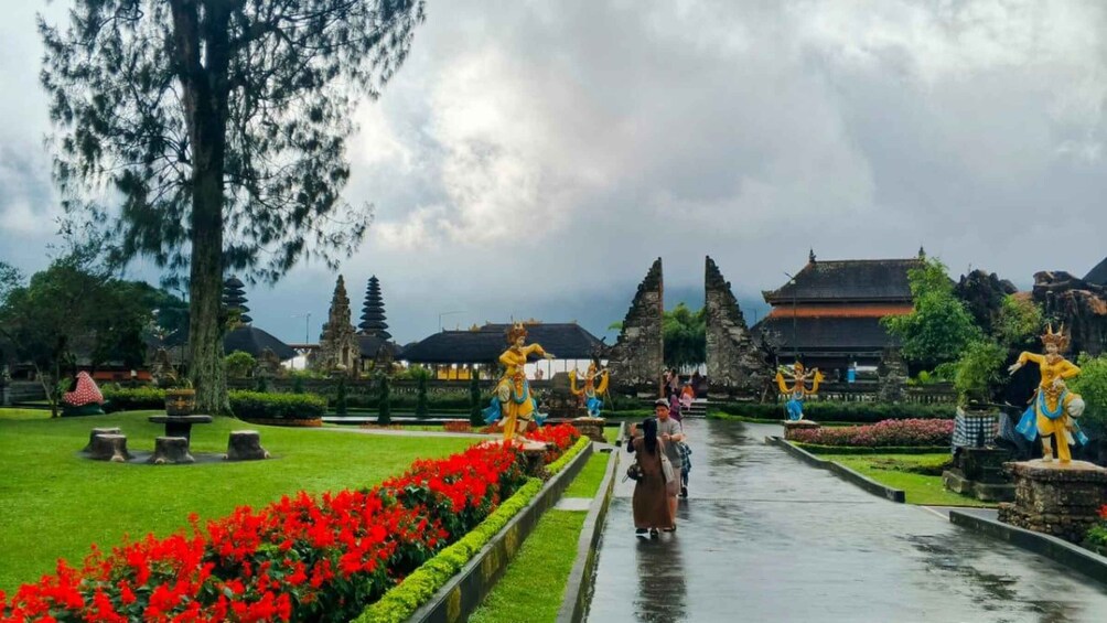 A temple complex with traditional architecture, a wet pathway, and statues. 1