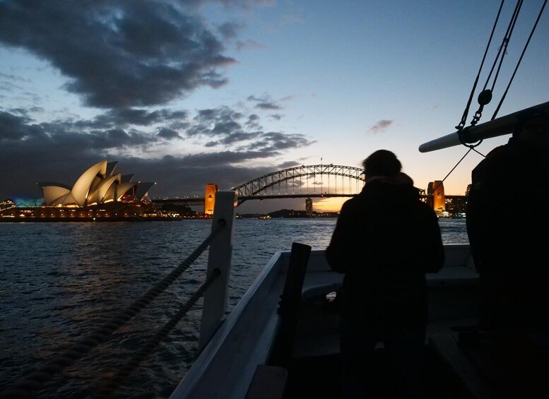 A silhouette of a person on a boat, the Sydney Opera House, and the Sydney Harbour Bridge at dusk. 4