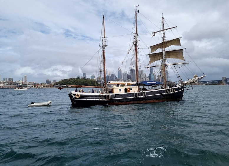 A large sailing ship with multiple masts and sails, docked in a harbor with a city skyline in the background. 1