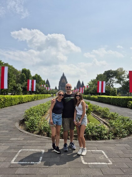 Three people standing on a paved pathway with red and white flags in the background. 2