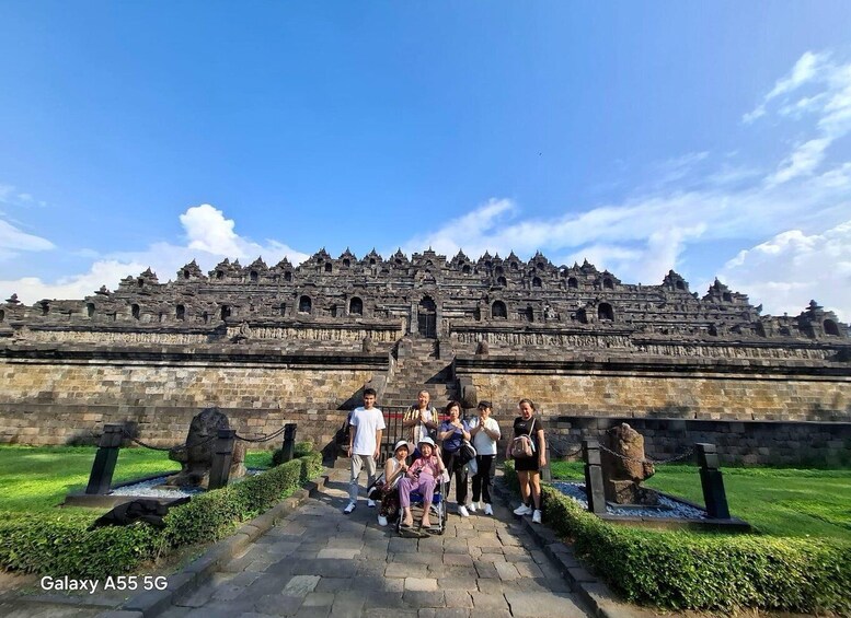 A group of people standing in front of a large, ancient stone structure with multiple levels and intricate carvings. 1
