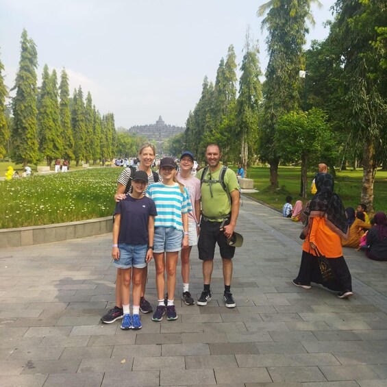 A group of people standing on a paved path in a park with trees and a distant hill. 5