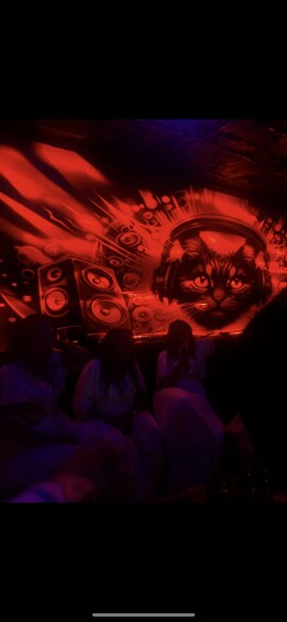 A room with a large cat illustration on the wall, surrounded by people sitting on chairs. 2