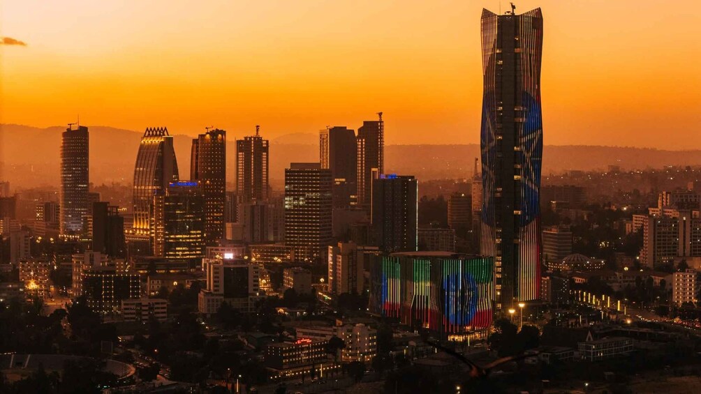 A cityscape at sunset with illuminated buildings and a prominent skyscraper with colorful lights. 4