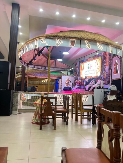A restaurant with a stage, tables, chairs, and a colorful sign. 5