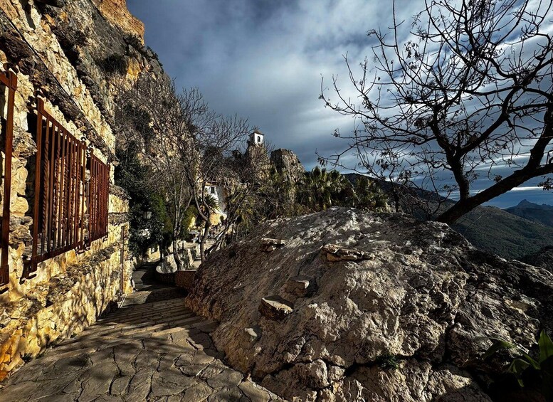 A stone pathway leading to a building with a metal gate, surrounded by rocky terrain and sparse vegetation. 5