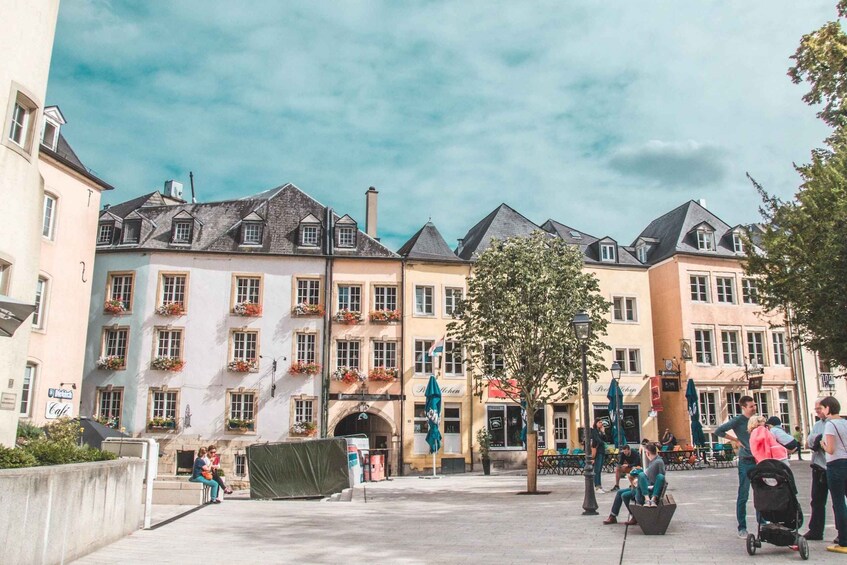 A European-style square with historic buildings, outdoor seating, and a tree. 1