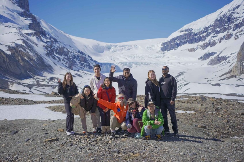 A group of people standing on a rocky terrain with snow-covered mountains in the background. 4