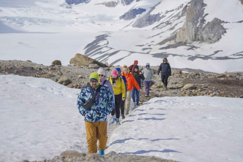 A group of hikers walking on a snow-covered trail with mountains in the background. 3