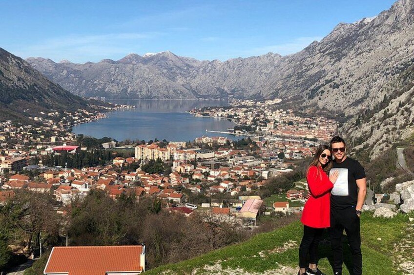 Una pareja está de pie en una colina con vistas a un pueblo, un lago y montañas al fondo. 4