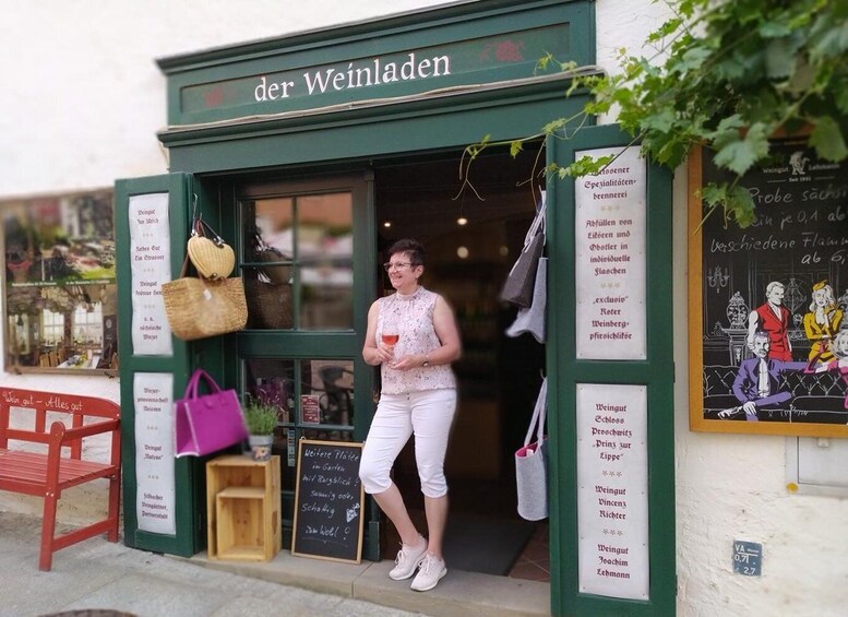 A woman exiting a shop named 'der Weinladen' with a drink in hand. 3