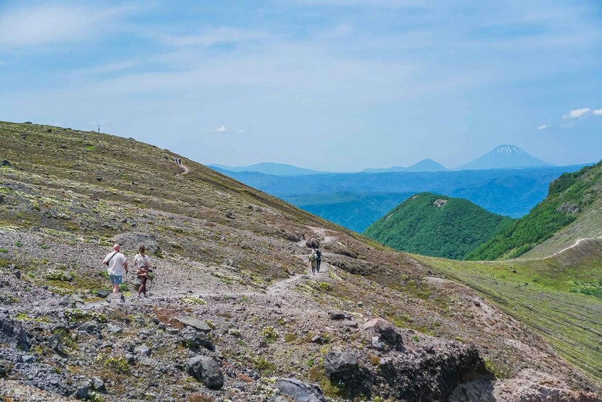 A mountainous landscape with hikers on a rocky trail and a distant mountain peak. 2
