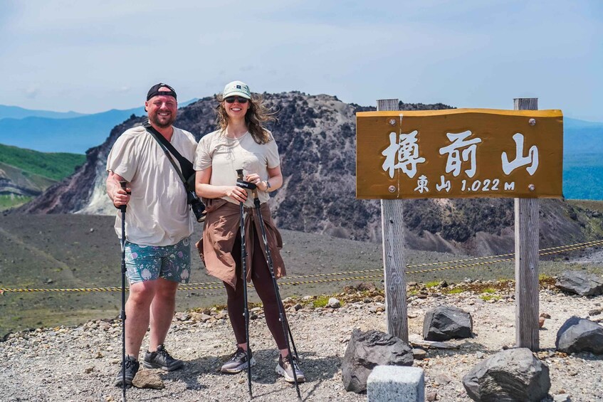 Two people standing on a rocky trail with a sign indicating a mountain peak at 1,022 meters. 3