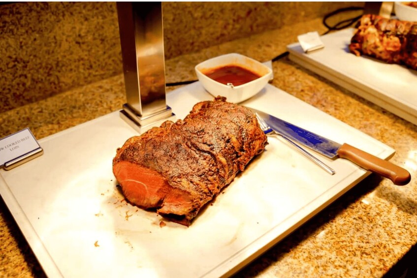 A cooked roast beef on a cutting board with a knife and a small bowl of sauce. 3