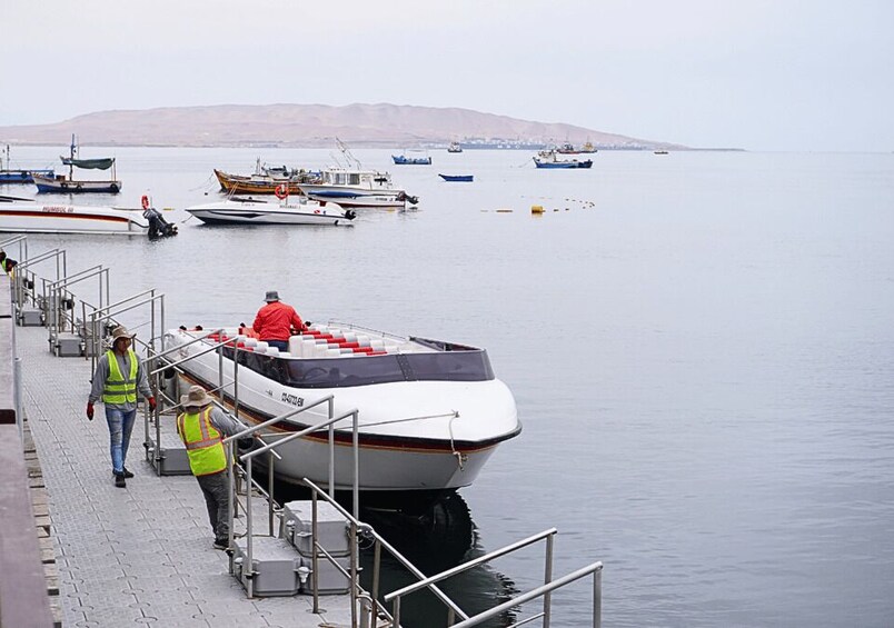 A dock with several boats, a person in a red jacket, and another in a safety vest. 2