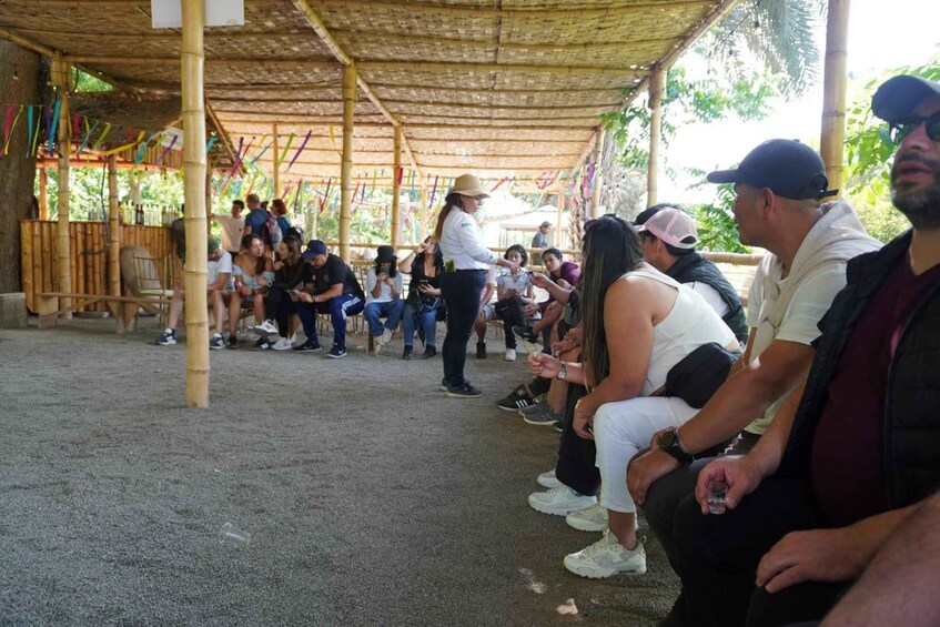 A group of people seated under a bamboo structure, some holding drinks, with a festive atmosphere. 4
