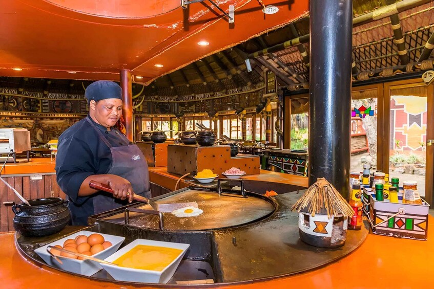 A street food vendor cooking on a griddle with a frying pan, a bowl of eggs, and a basket of oranges. 5