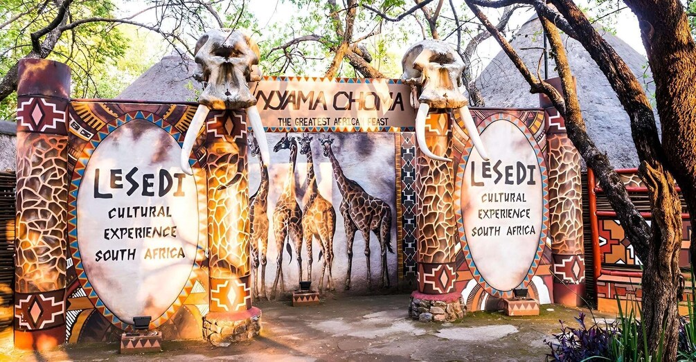 A gate with giraffe sculptures and text promoting Lesedi Cultural Experience in South Africa. 4