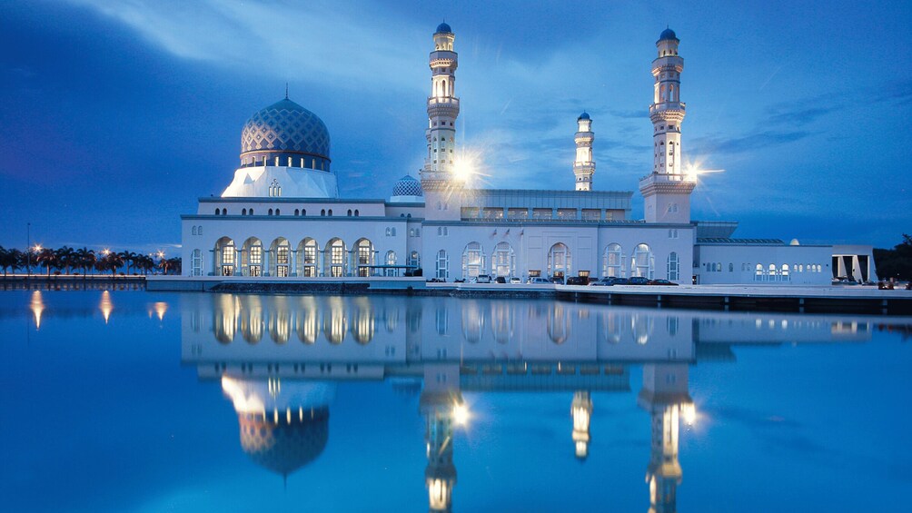 A mosque with three minarets and a large dome, reflecting in calm water. 1