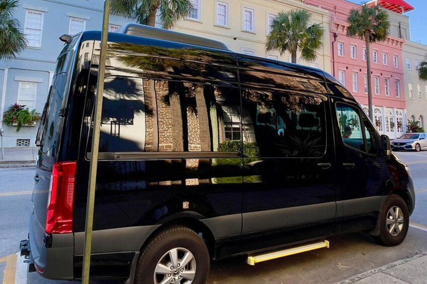 A black van parked on a street with palm trees and colorful buildings in the background. 4