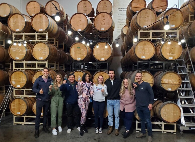 A group of people standing in front of stacked wooden barrels in a warehouse. 3