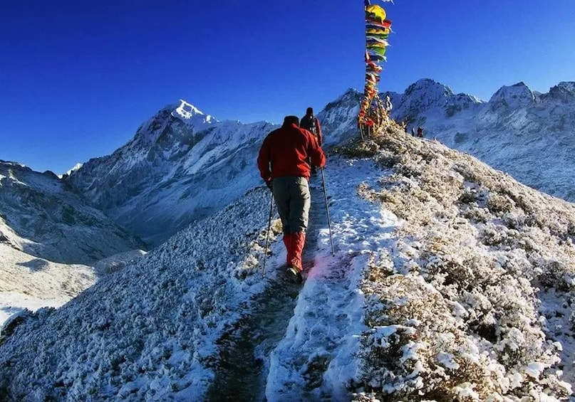 A person hiking on a snow-covered mountain trail with a prayer flag line. 3